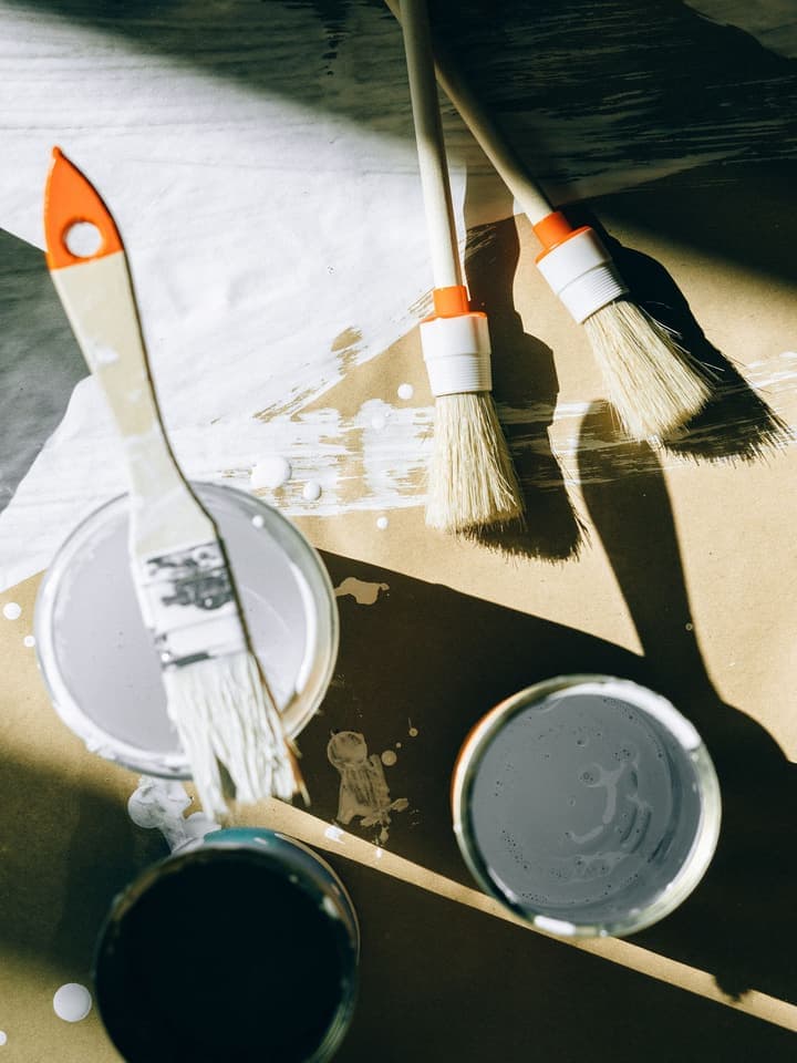 Latas de tinta abertas com pincéis e trincha sobre papel de proteção, material de pintura vendido na Progresso em Aparecida de Goiânia